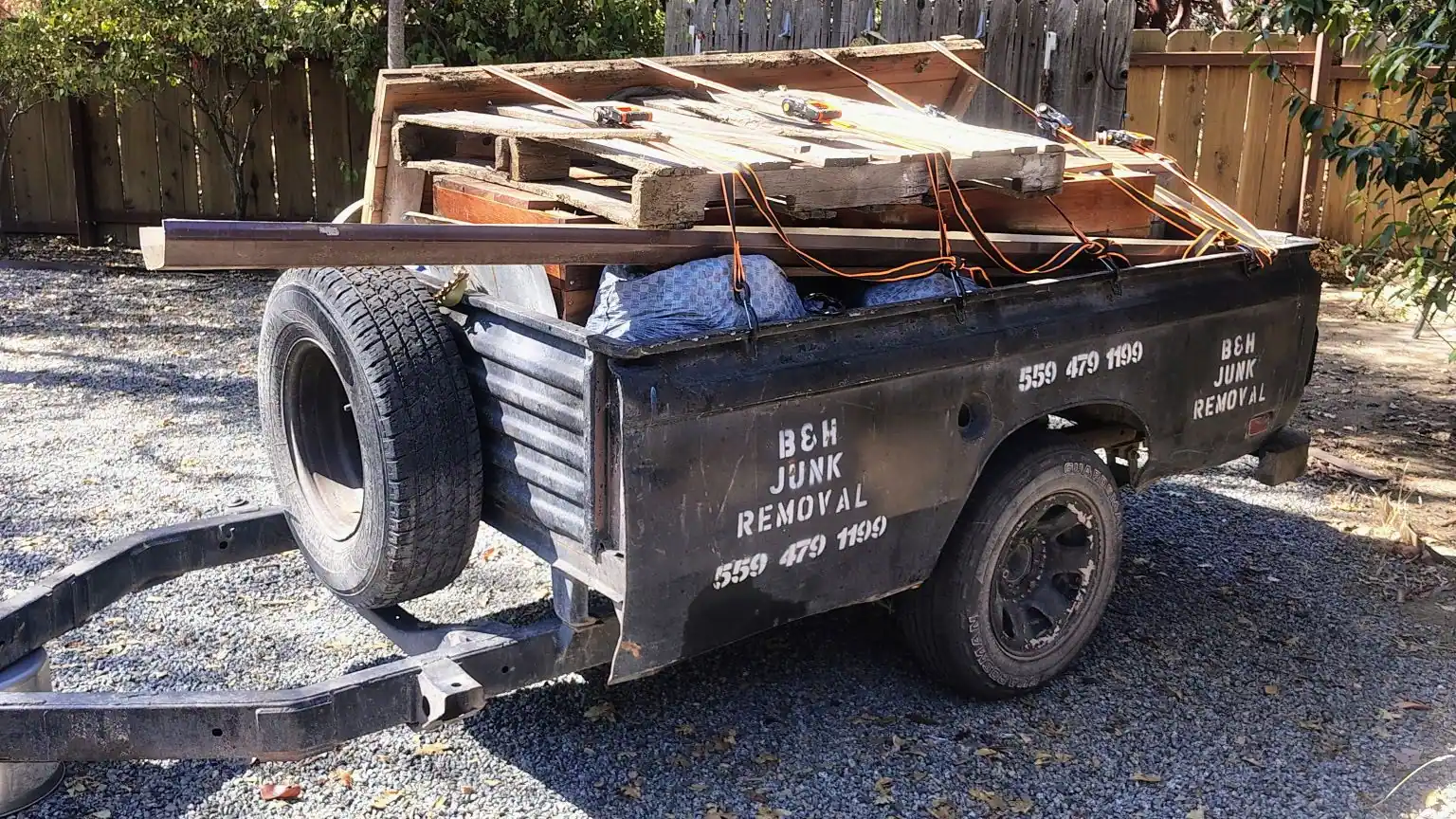 The B&H Junk Removal trailer loaded with pallets and cut lumber; strapped down