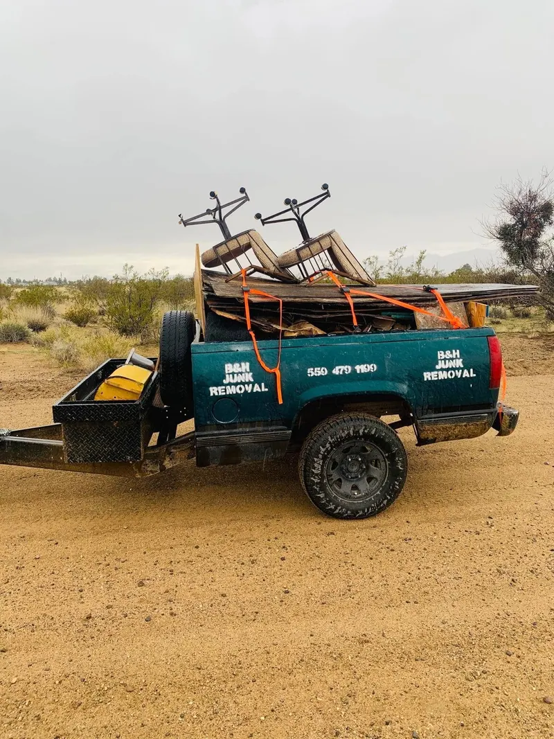 The B&H Junk Removal pickup loaded with old boards and two bar stools on open desert ground