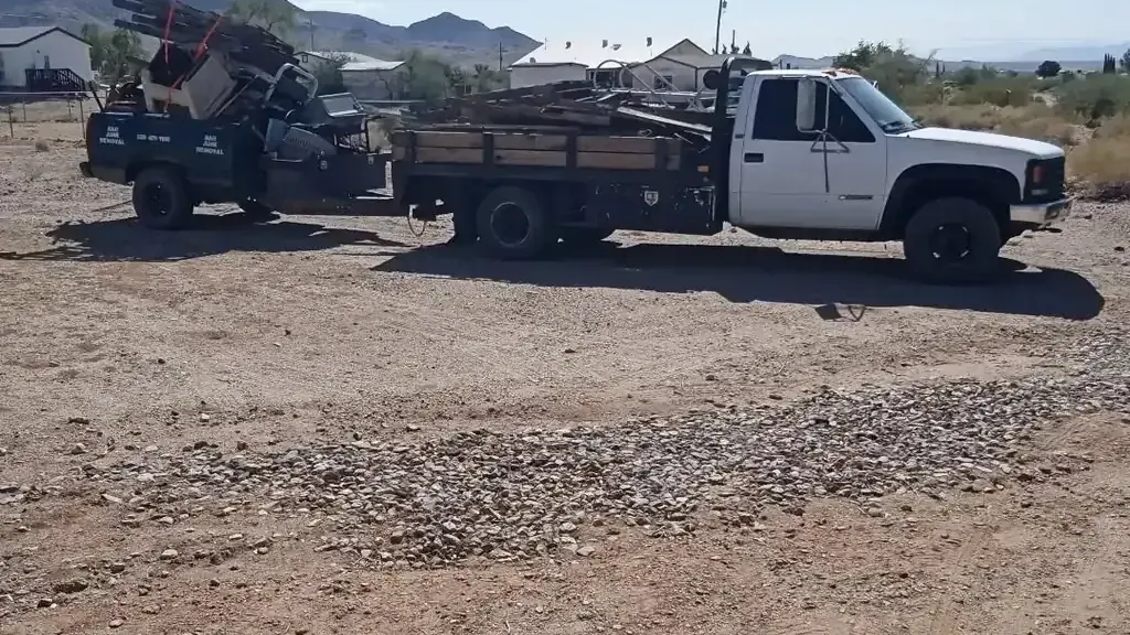 A flatbed truck and a truck bed trailer both loaded with old lumber