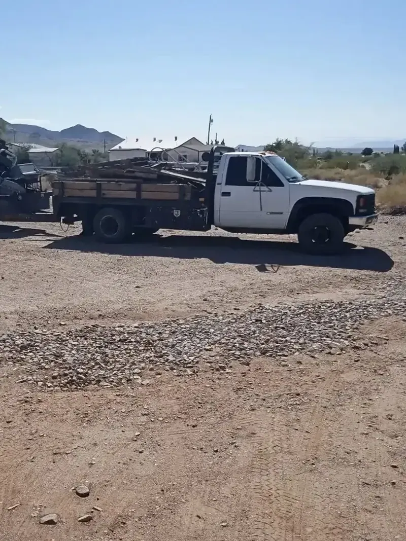 A flatbed truck and a truck bed trailer both loaded with old lumber