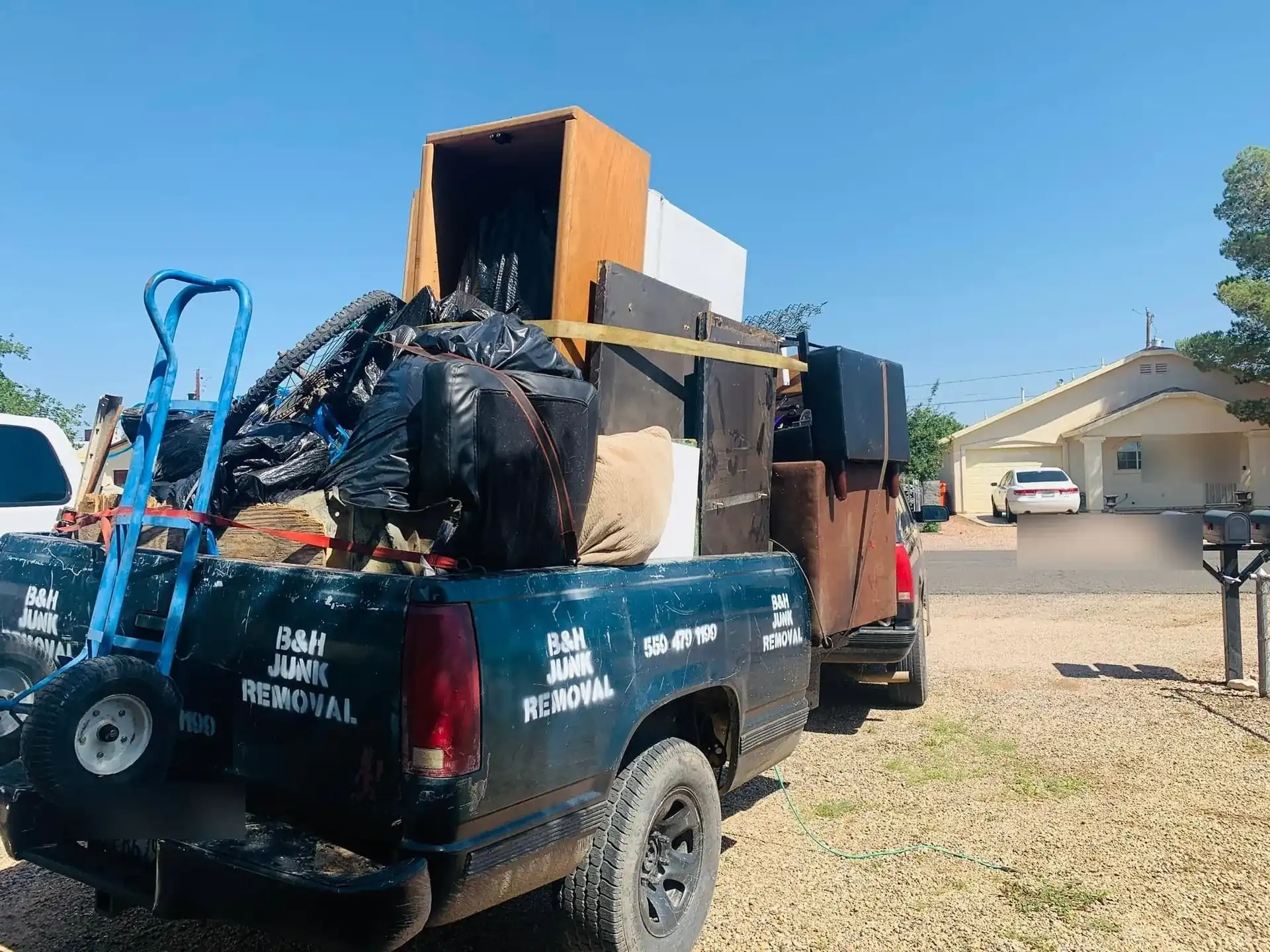 The B&H Junk Removal truck and trailer loaded with furniture and bagged waste