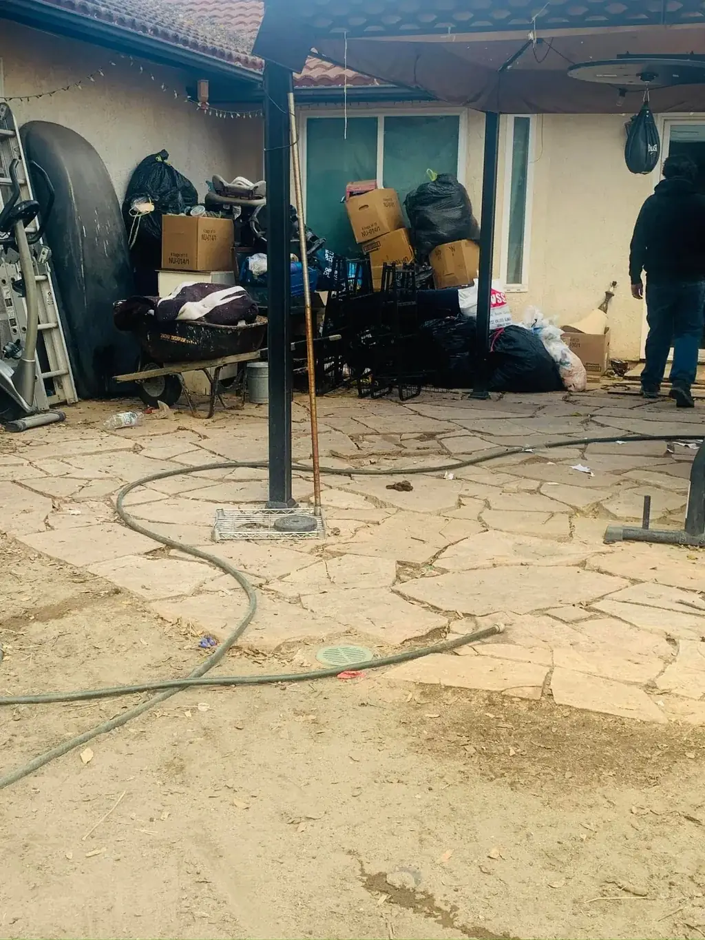 A patio cluttered with exercise equipment, a ladder and a wheelbarrow