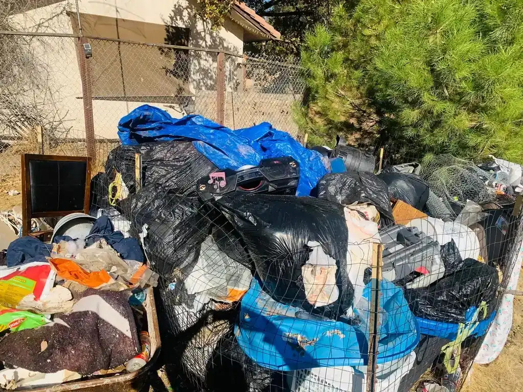 A large pile of bagged waste and household junk stacked against a fence
