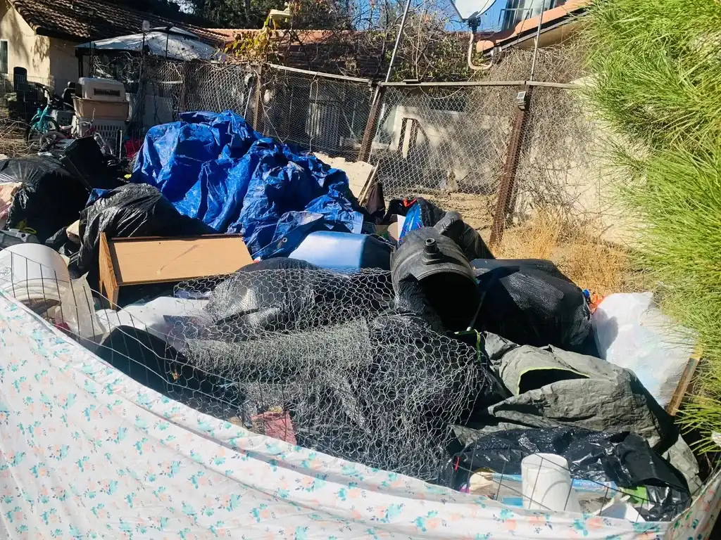 A cleanout pile with a mattress, tarps, rolled wire fencing and a dresser