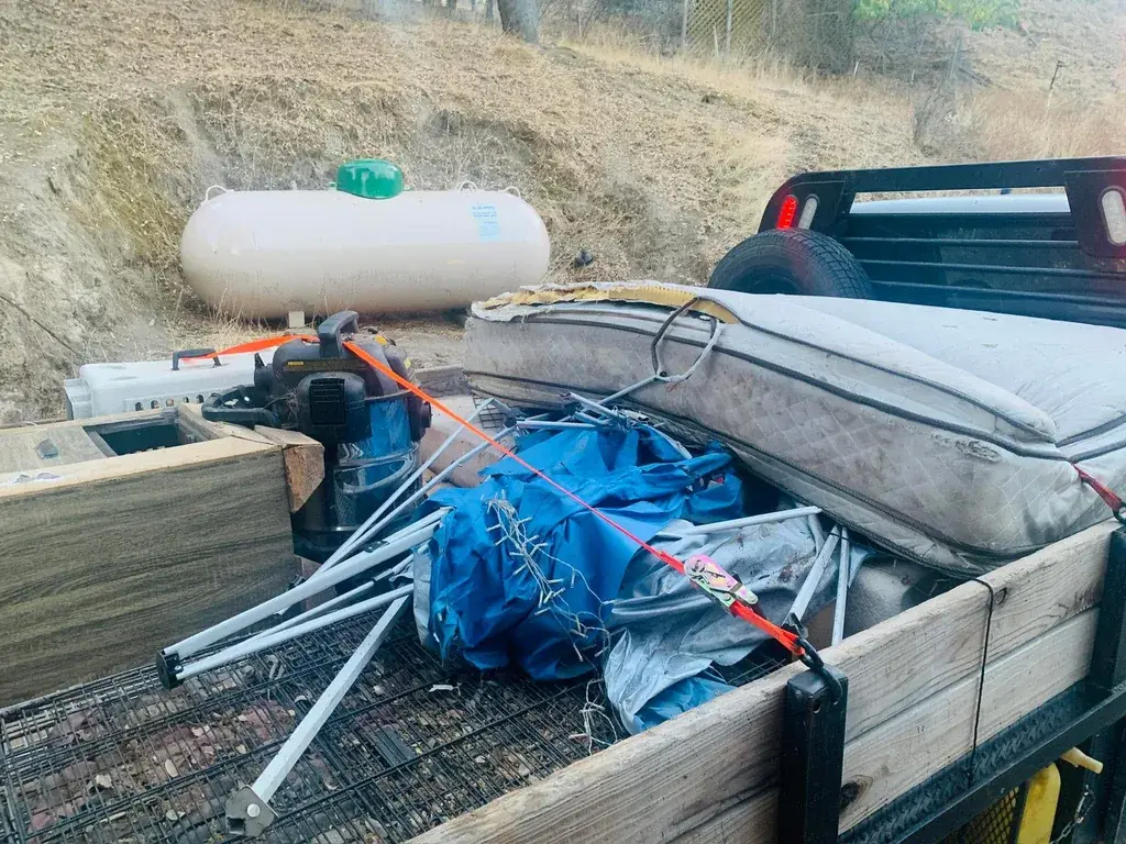A trailer loaded with a mattress, a pool cover and yard items