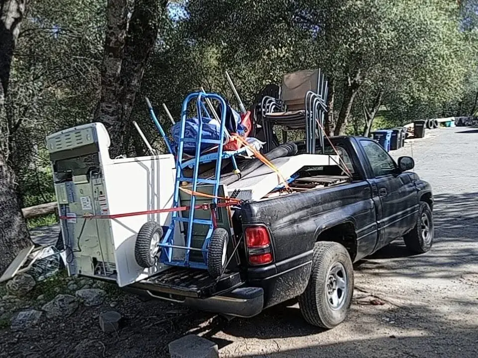A pickup loaded with an old appliance, stacking chairs and a hand truck