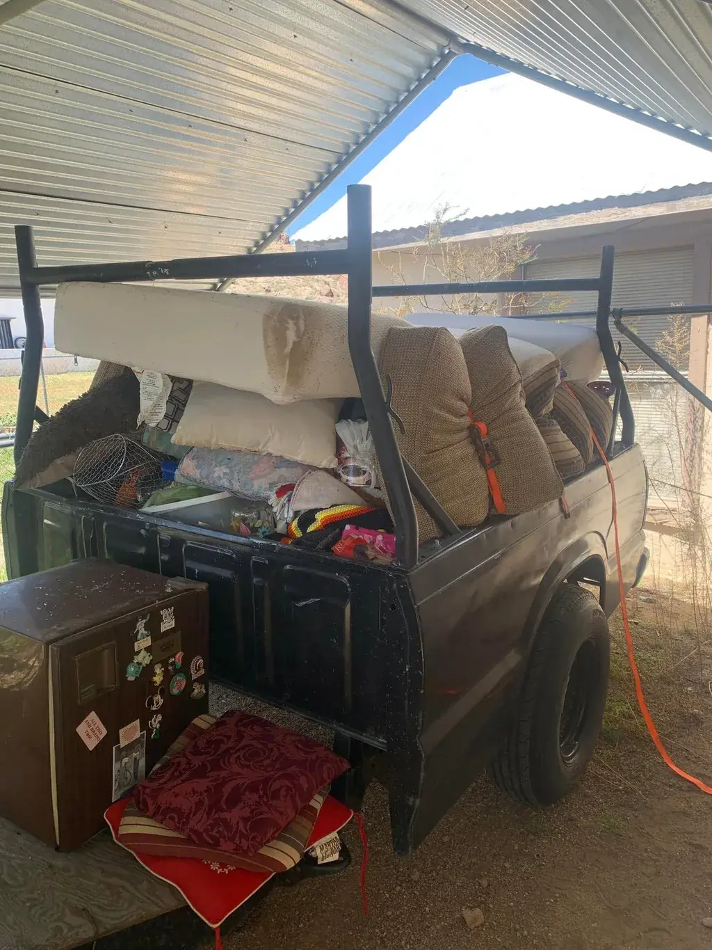 A truck bed loaded with a mattress, cushions and a small fridge