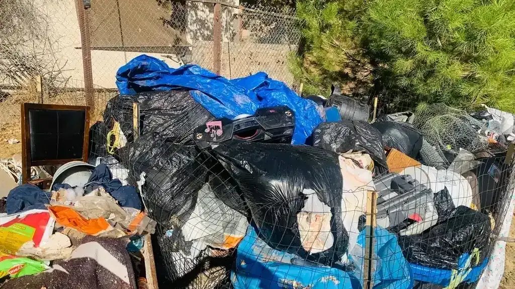 A large pile of bagged waste and household junk stacked against a fence