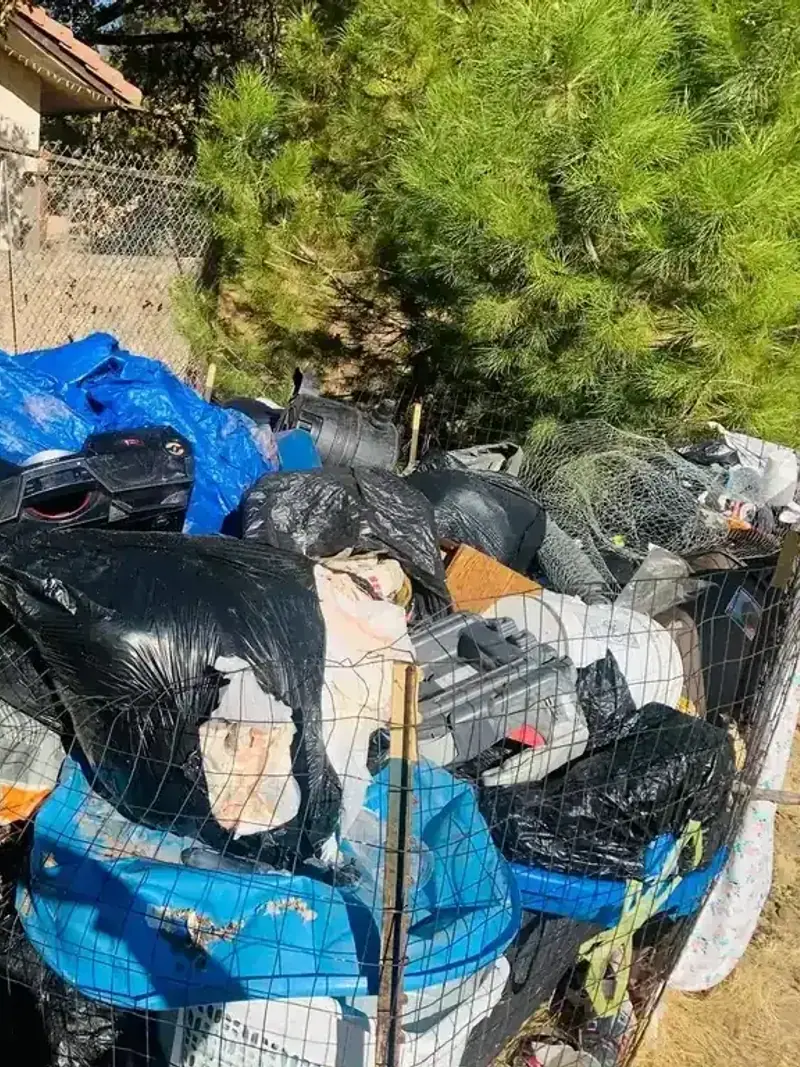 A large pile of bagged waste and household junk stacked against a fence
