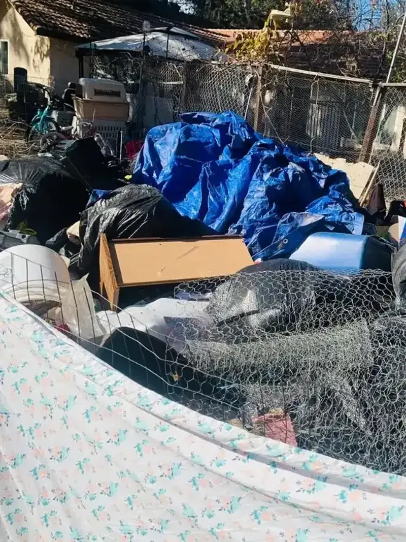 A cleanout pile with a mattress; tarps; rolled wire fencing and a dresser