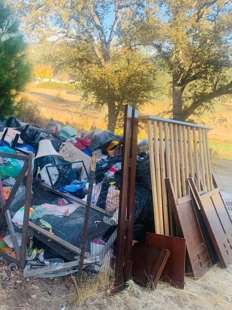 A long heap of bagged waste; bed frames and boxed household goods stacked at the edge of a lot