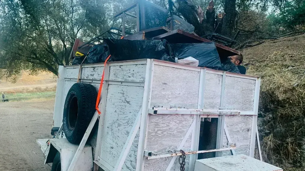 A trailer loaded above the sides with furniture; bagged waste and scrap wood