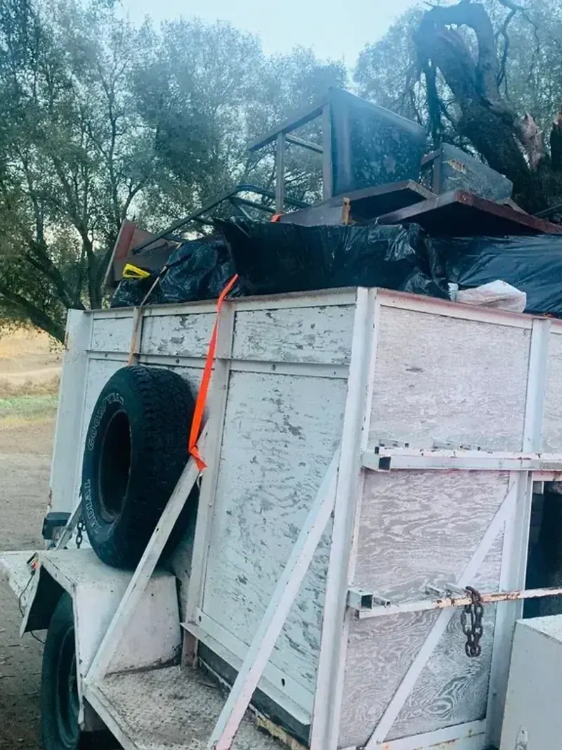 A trailer loaded above the sides with furniture; bagged waste and scrap wood