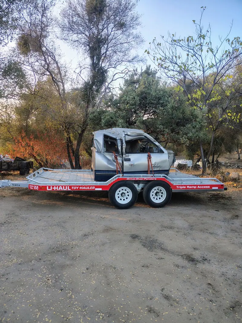A wrecked pickup cab strapped down on a flatbed trailer ready to be hauled away