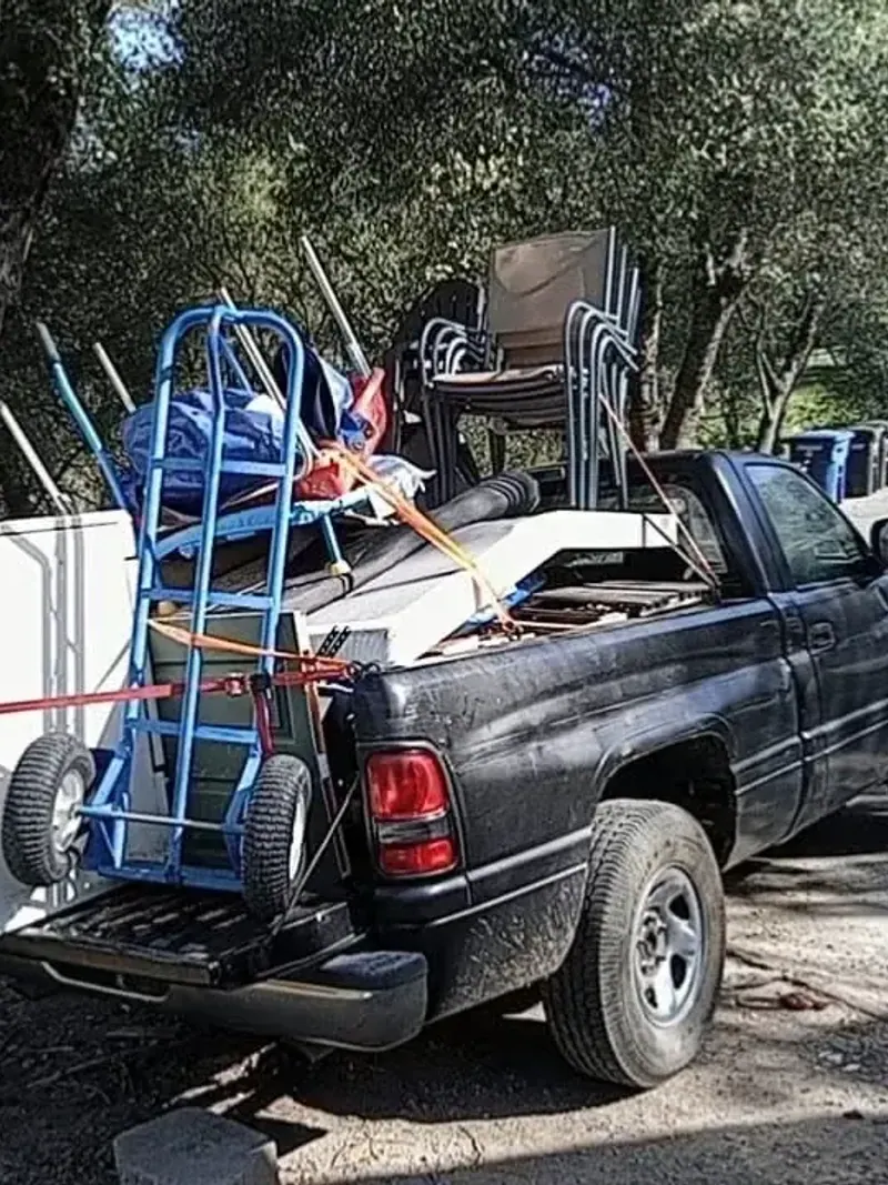 A pickup loaded with an old appliance; stacking chairs and a hand truck