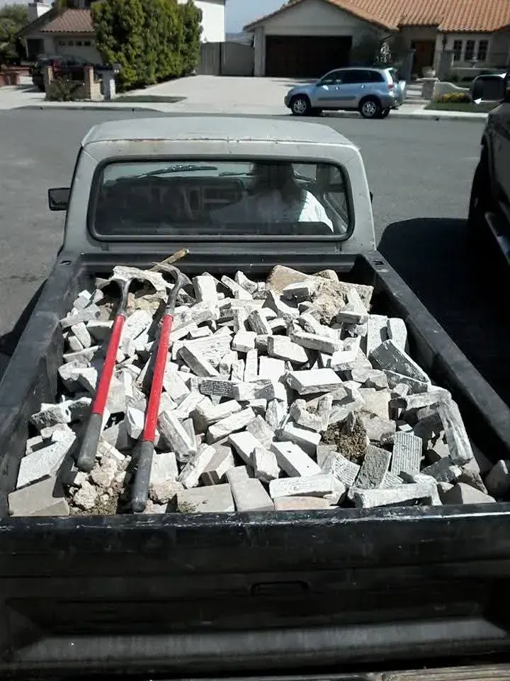 A truck bed loaded with broken concrete; brick and two sledgehammers