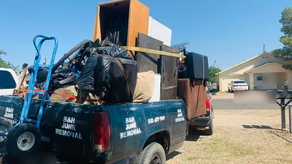 The B&H Junk Removal truck and trailer loaded with furniture; a cabinet and bagged waste