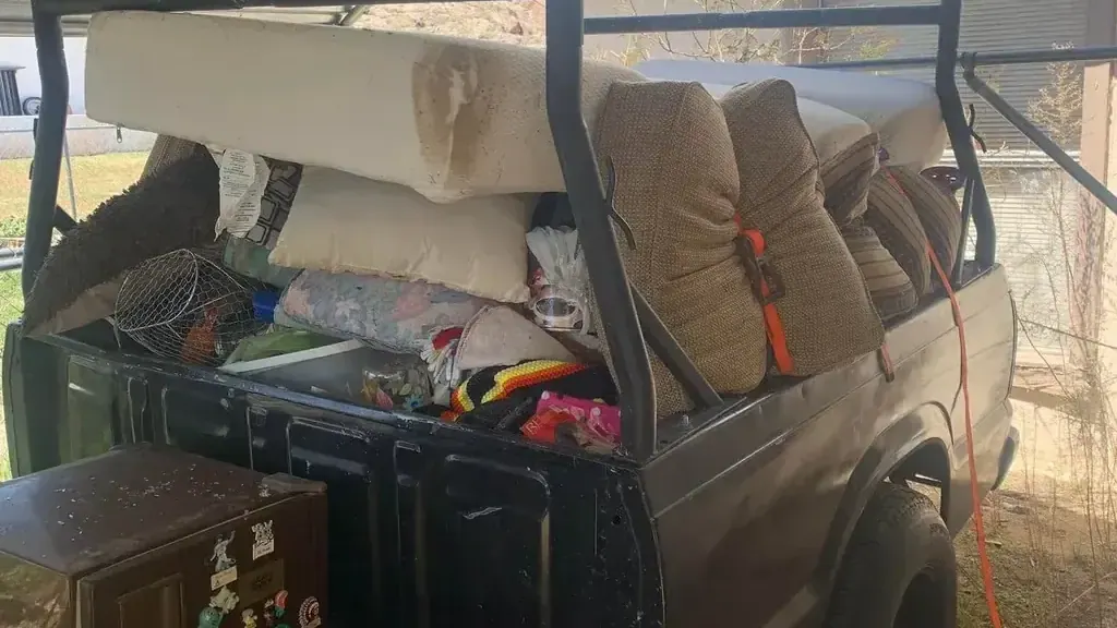 A truck bed loaded with a mattress; cushions and a small fridge