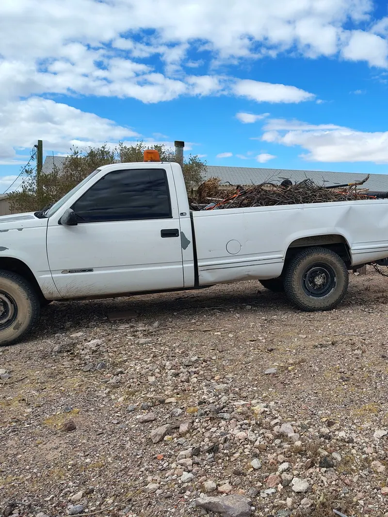 The pickup and a towed trailer bed both loaded with dead brush and cut branches on a desert lot